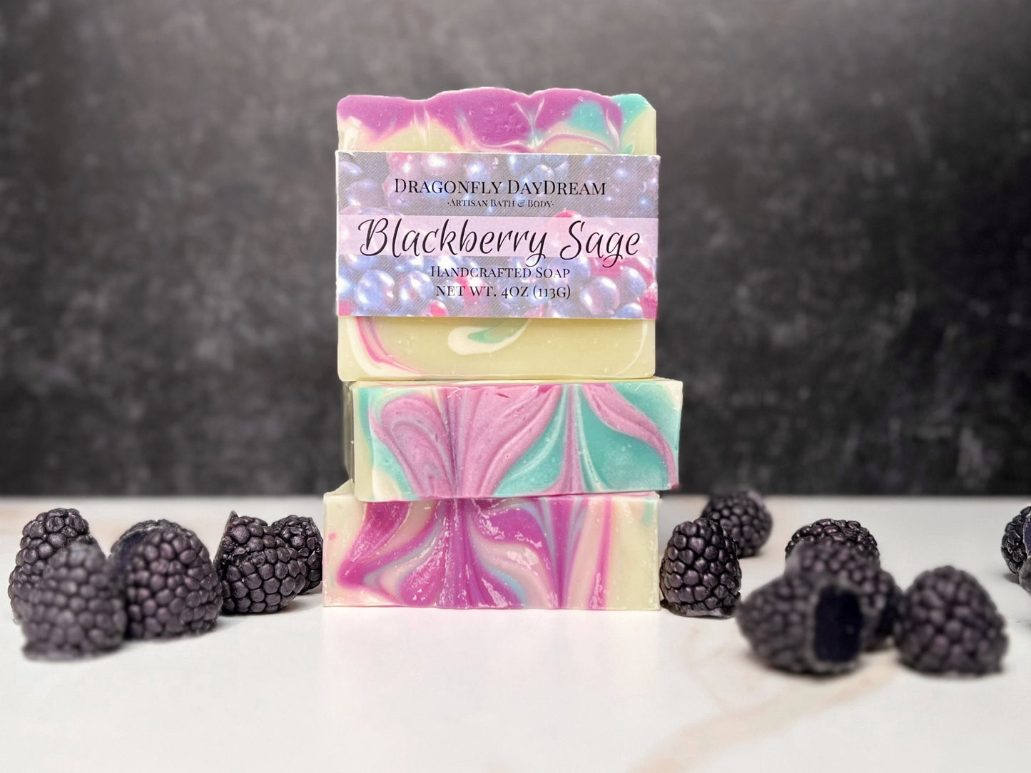 Stack of three soaps. Soaps swirled with green & purple. Soap "blackberrys" are on table surrounding soap stack.