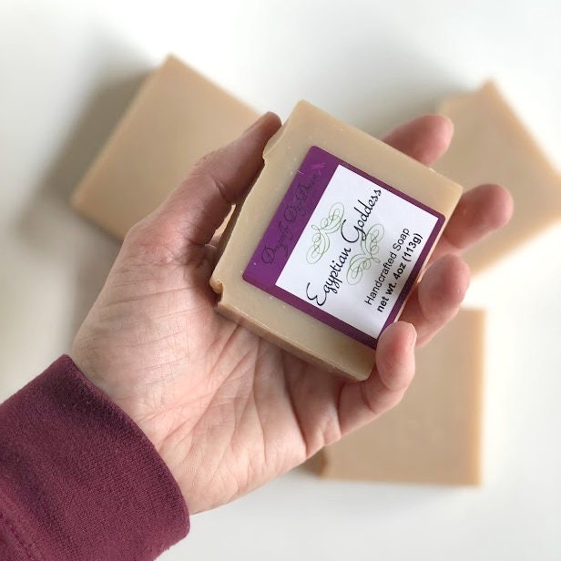 Egyptian Goddess tan soap labeled and held in hand for size comparison, with three blurred tan soaps in the background against a white backdrop.