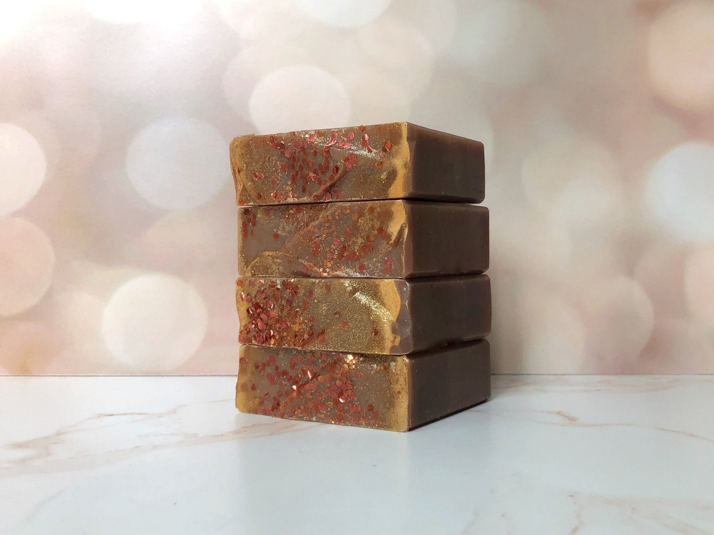 Stack of 4 myrrh and frankincense soaps. Soaps have a dark golden eco-glitter. Set on marble countertop and blurred fairly lights in background