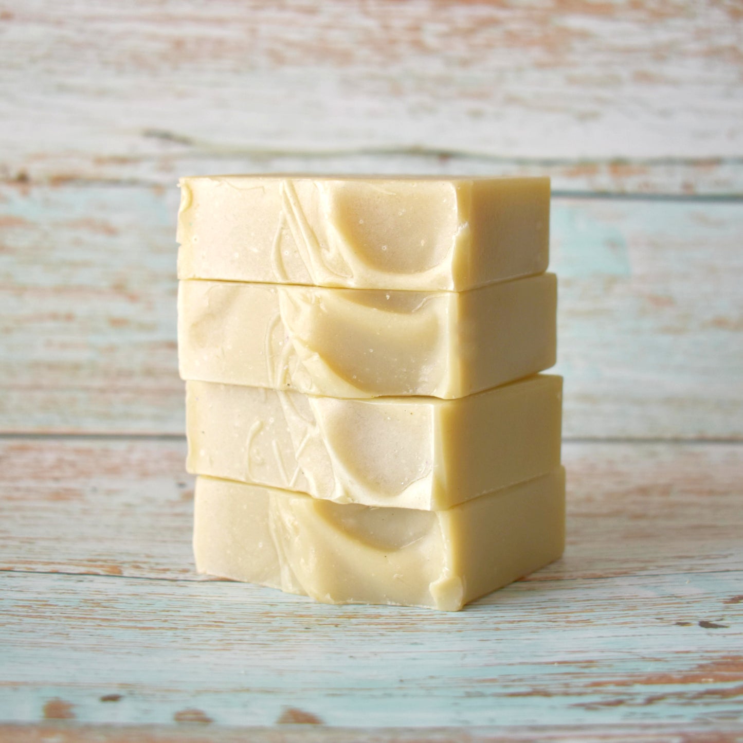 Stack of 4 rectangular beige soaps showcasing the tops of the soaps sitting on a weathered light blue wooden background