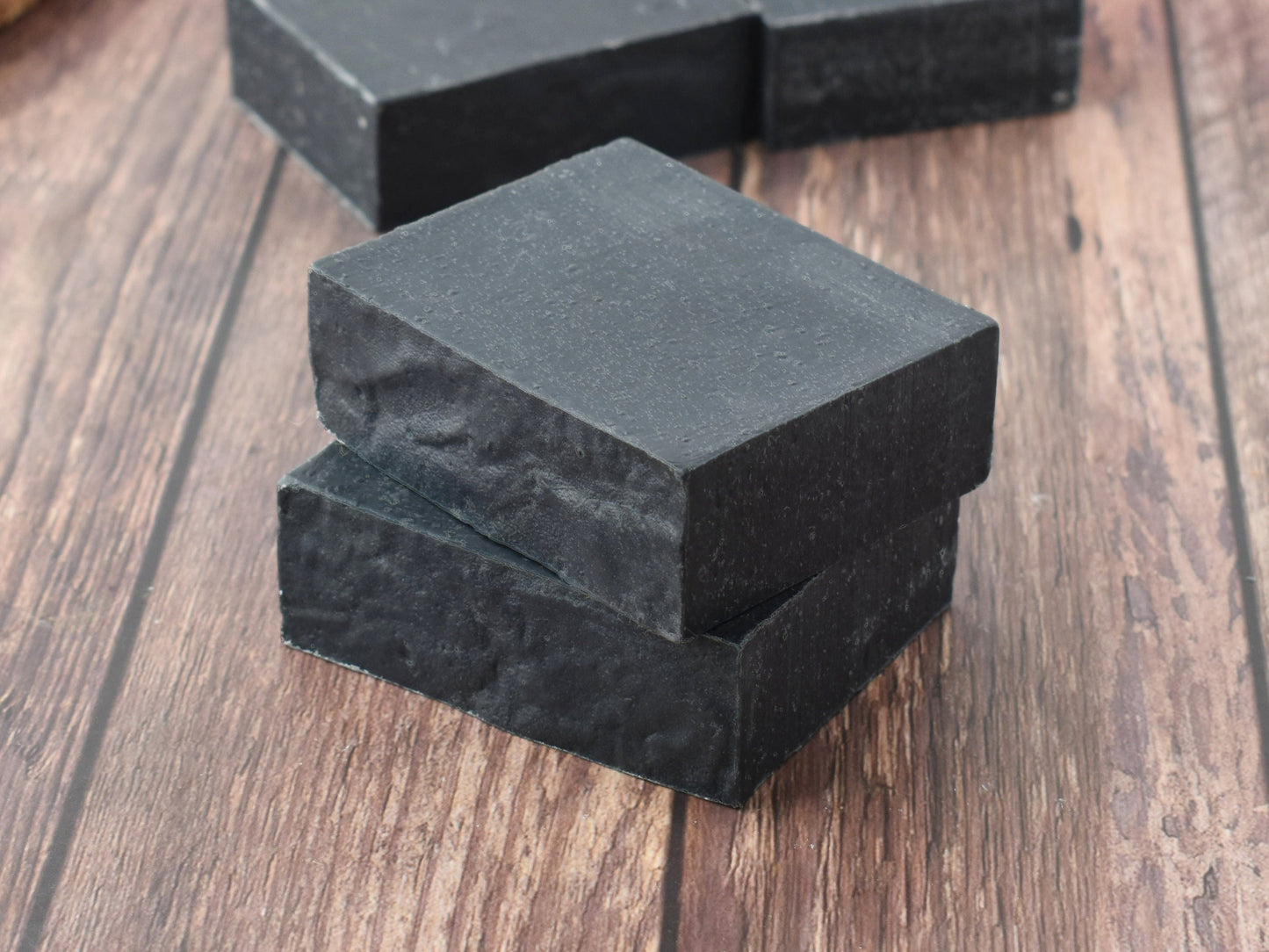 Black charcoal soap stacked on a medium brown wood table