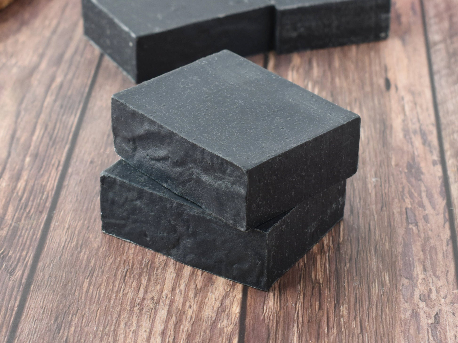 Black charcoal soap stacked on a medium brown wood table