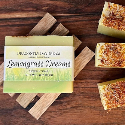 One bar of Lemongrass Dreams soap ontop of a reclaimed slatted wood soap tray.  Three more Lemongrass dream soaps on on the sidelines showing the orange safflower herbs on top