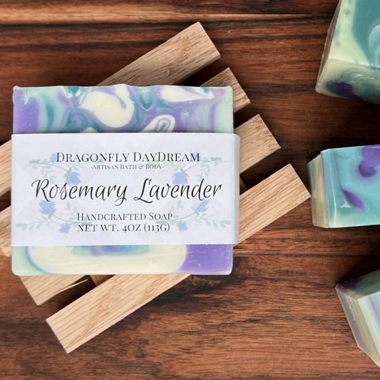 Rosemary Lavender Handcrafted Soap, Dragonfly DayDream, Artisan Bath & Body, Net Wt. 4oz (113g).  Soap  is sea foam green with white, dark green and purple swirls.  Soap is on a wooden slatted tray sitting on a dark brown wooden table.  Three additional soaps are off to the right to show top.