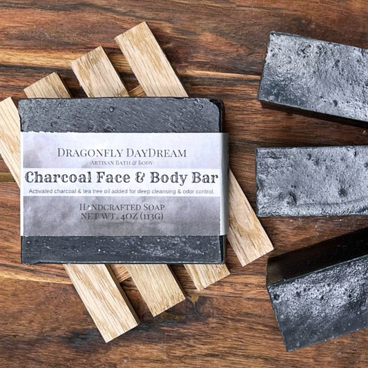 Labelled black charcoal soap on recycled wood tray, with three additional charcoal soaps on dark brown background.