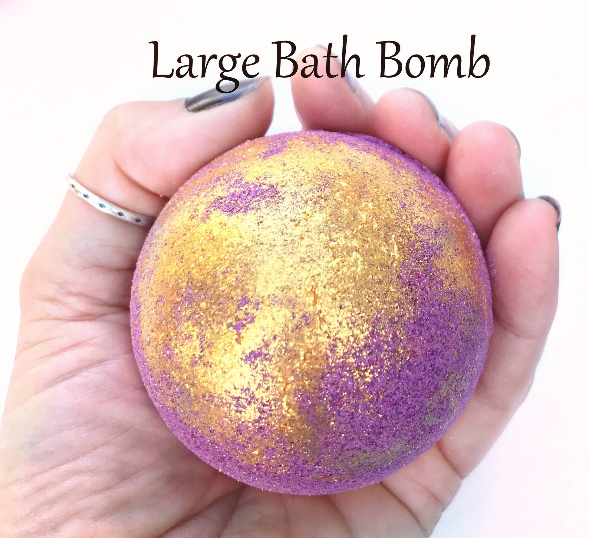 Eclipse bath bomb (purple with gold eco-glitter) held in hand to show size.  "large bath bomb" in writing on photo
