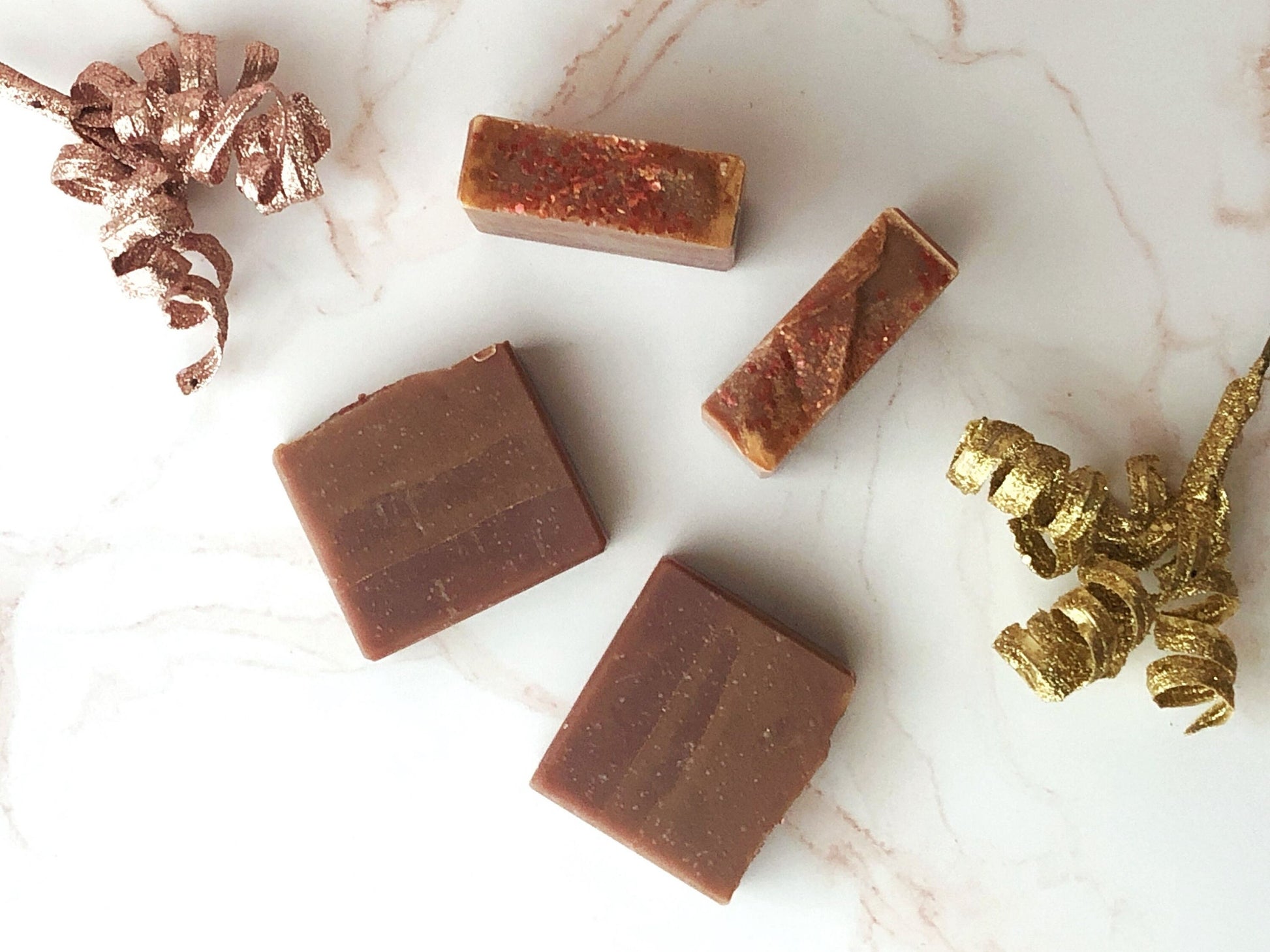 4 bars of myrrh and frankincense soap on a marble countertop with two festive gold and rose gold streamers.