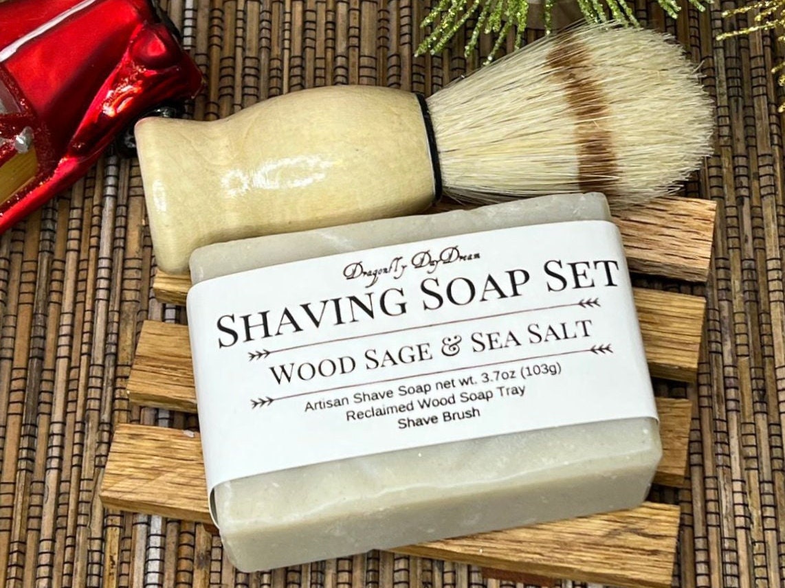 Shaving soap, shaving brush, and reclaimed wood soap tray arranged on a grass mat. A red truck ornament and a sparkly green tree adorn the top of the photo.